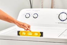 Front-loading washing machine being leveled with a bubble level tool on top, ensuring stability for longer appliance life