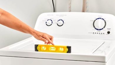 Front-loading washing machine being leveled with a bubble level tool on top, ensuring stability for longer appliance life