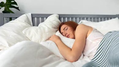 Woman sleeping peacefully on LOFE organic buckwheat pillow with calm expression and open window showing fresh air