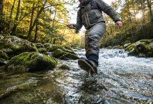 An angler wearing specialized wading boots while standing on slippery river rocks.