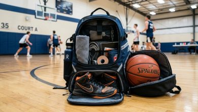 Black athletic backpack with a basketball and sneaker compartment against a wall.