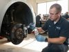 Male mechanic applying ceramic grease to car brakes in a sunlit workshop.