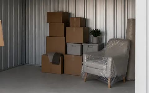 Stacked cardboard boxes and a plastic-wrapped armchair stored inside a self storage unit